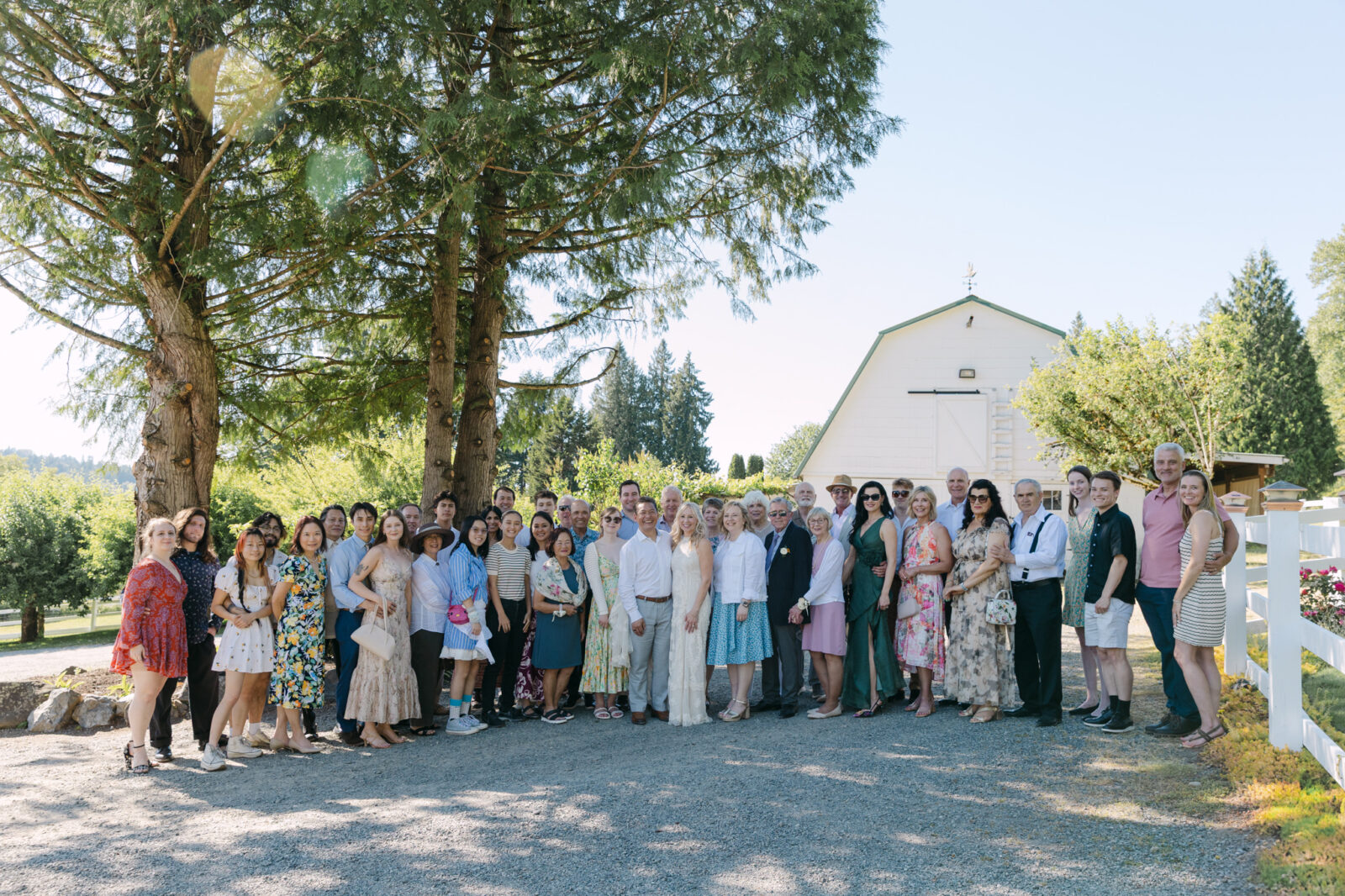 Wedding guests posing for a large group photo in front of the white barn at Chateau Lill.