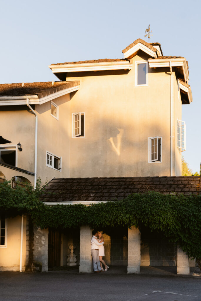 Bride and groom holding each other beneath greenery outside Chateau Lill.
