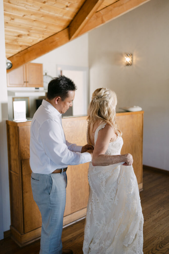 Groom helping bride button her wedding dress during getting ready photos at Chateau Lill.