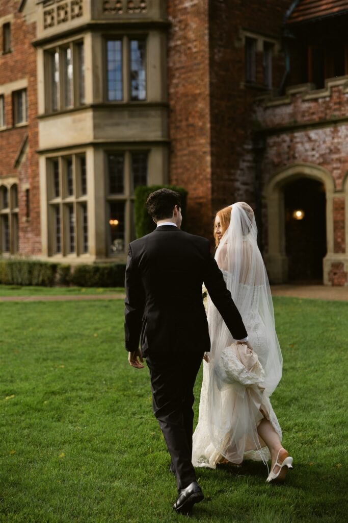 Bride and groom walking outdoor on the lawn in front of Thornewood Castle.