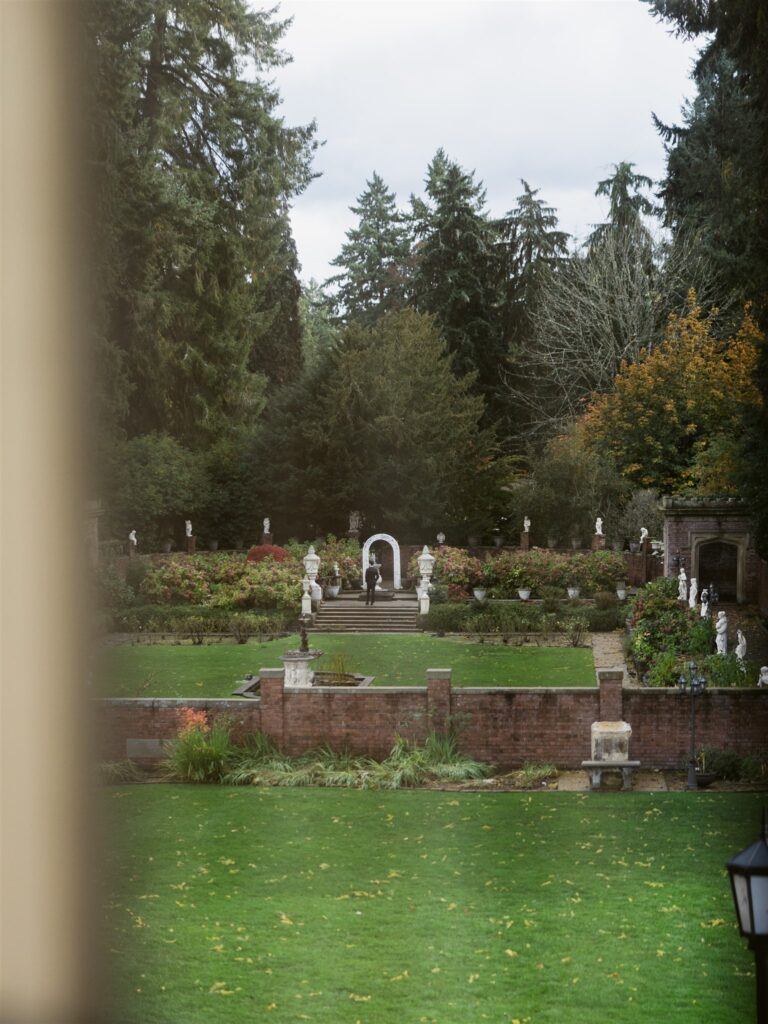 Far away shot through at window of the bride and groom meeting in the Sunken Garden for their first look at Thornewood Castle wedding venue,