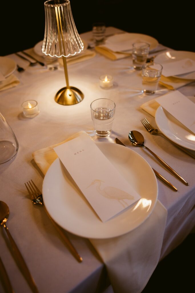 Indoor wedding reception table setup with menu, romantic lighting, and glasses.