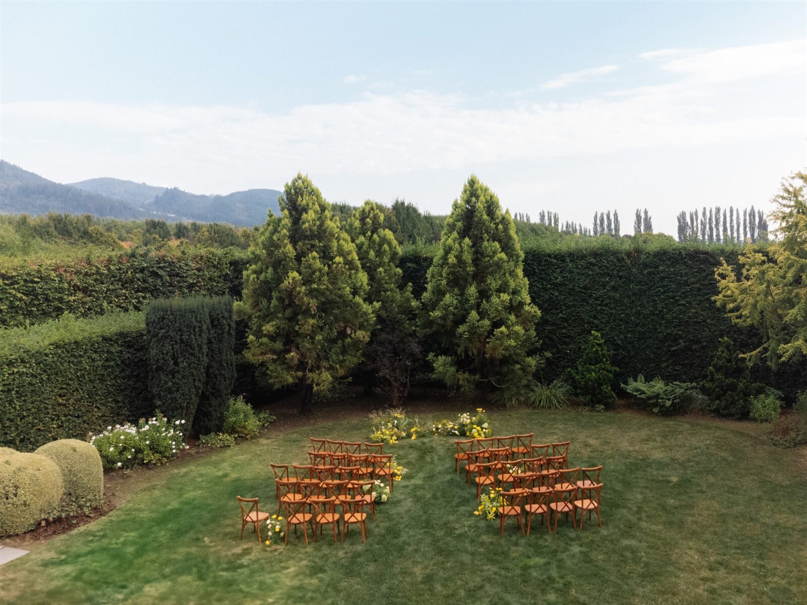 Drone shot of a Briarwood Estate wedding ceremony setup with wooden chairs and yellow floral arrangements in garden setting.