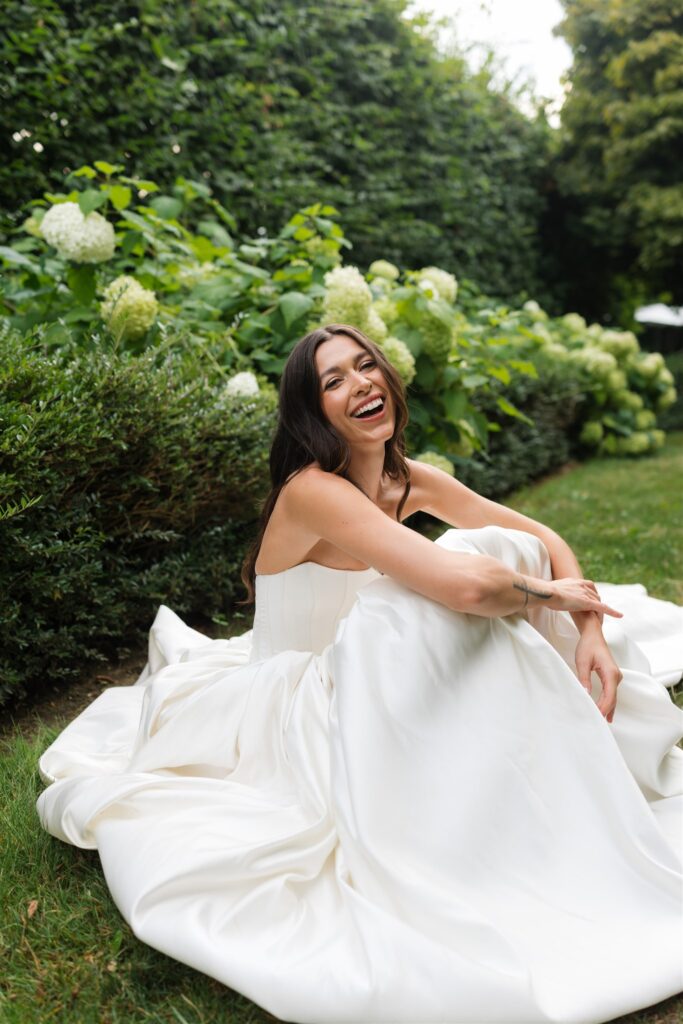 Candid photo of a bride laughing while sitting in a garden space.
