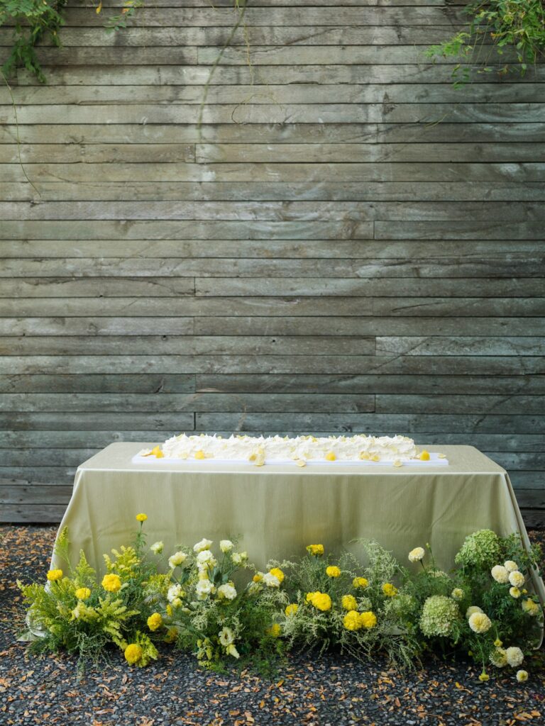 Wedding reception cake and table decorated with yellow blooms in front.