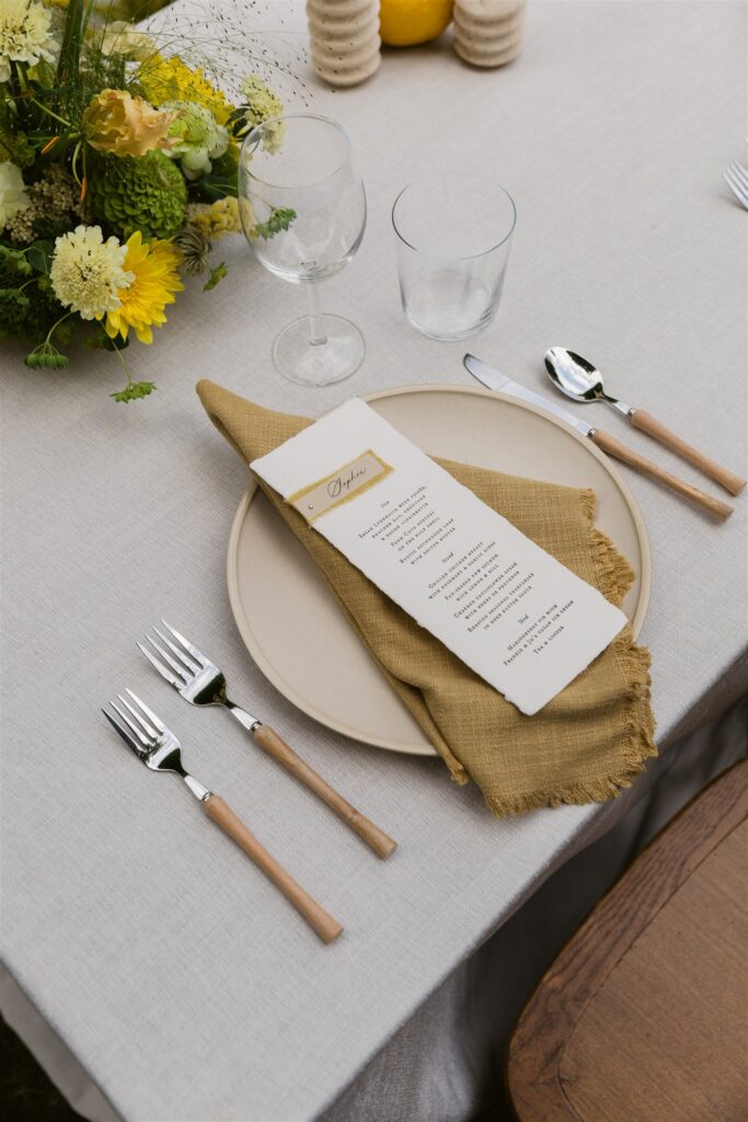 Close up of wedding place setting with menu, linen napkin, and wood flatware.