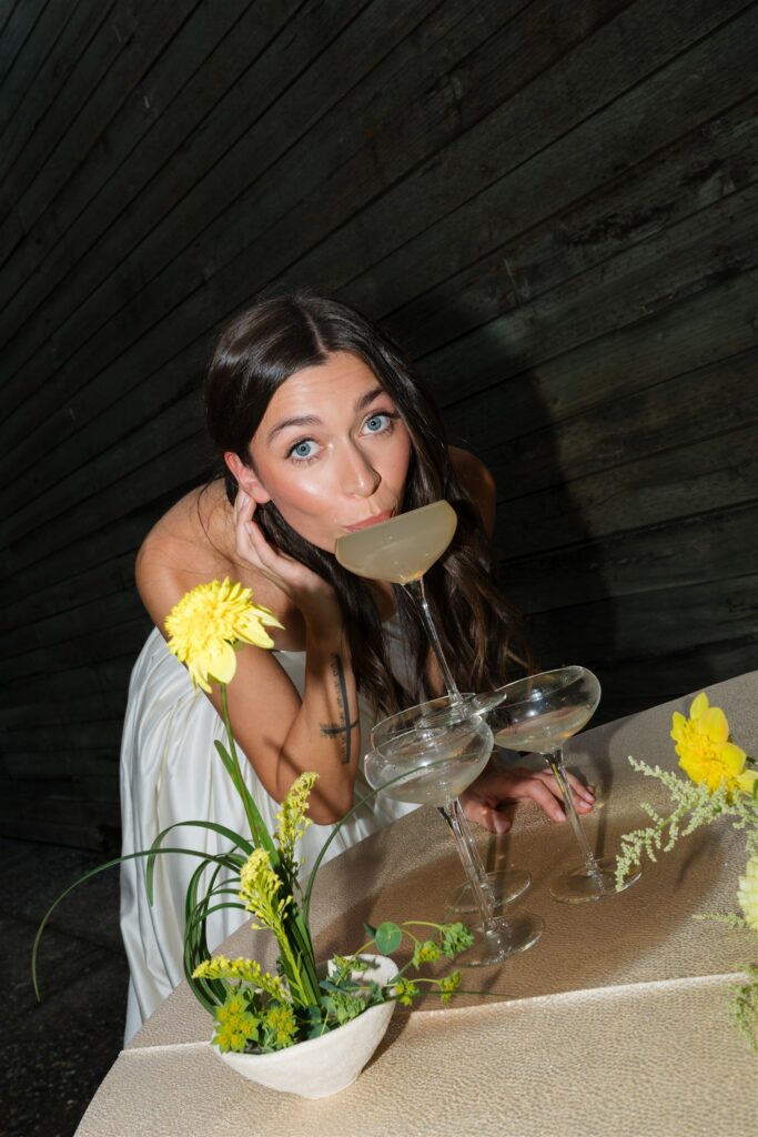 Bride drinking cocktail at reception table with floral details at Briarwood Estate wedding.