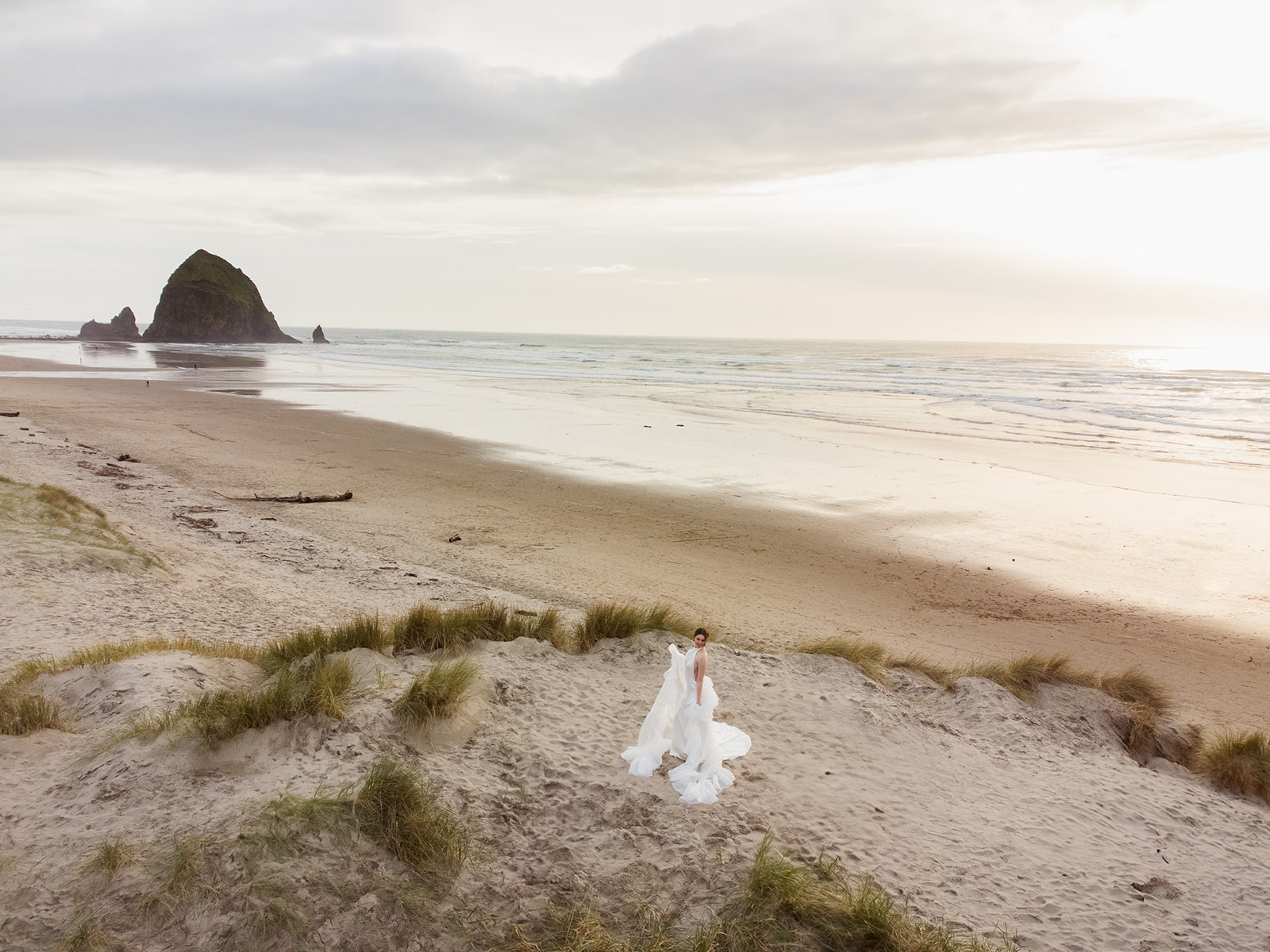 Drone shot of a bride posing on Cannon Beach with Haystack Rock in the distance.