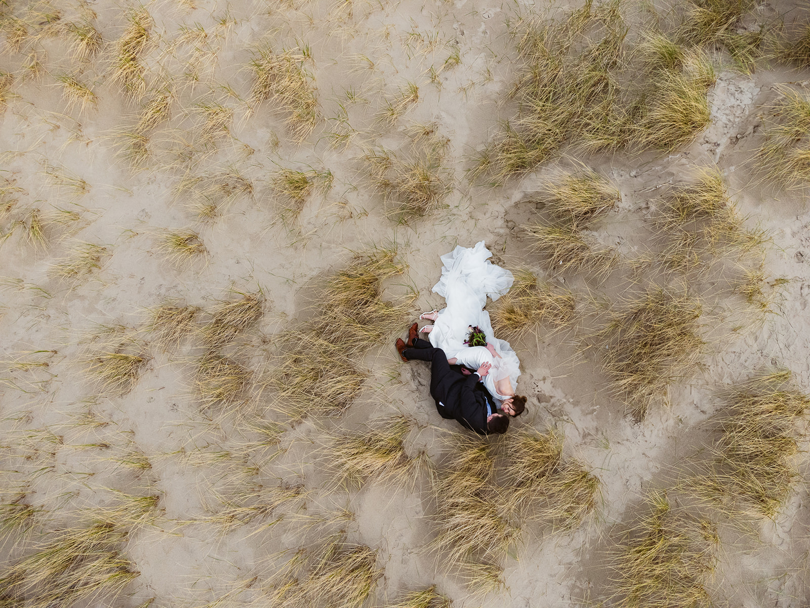 Overhead drone shot of a bride and groom laying in the beach grass during their Cannon Beach elopement.