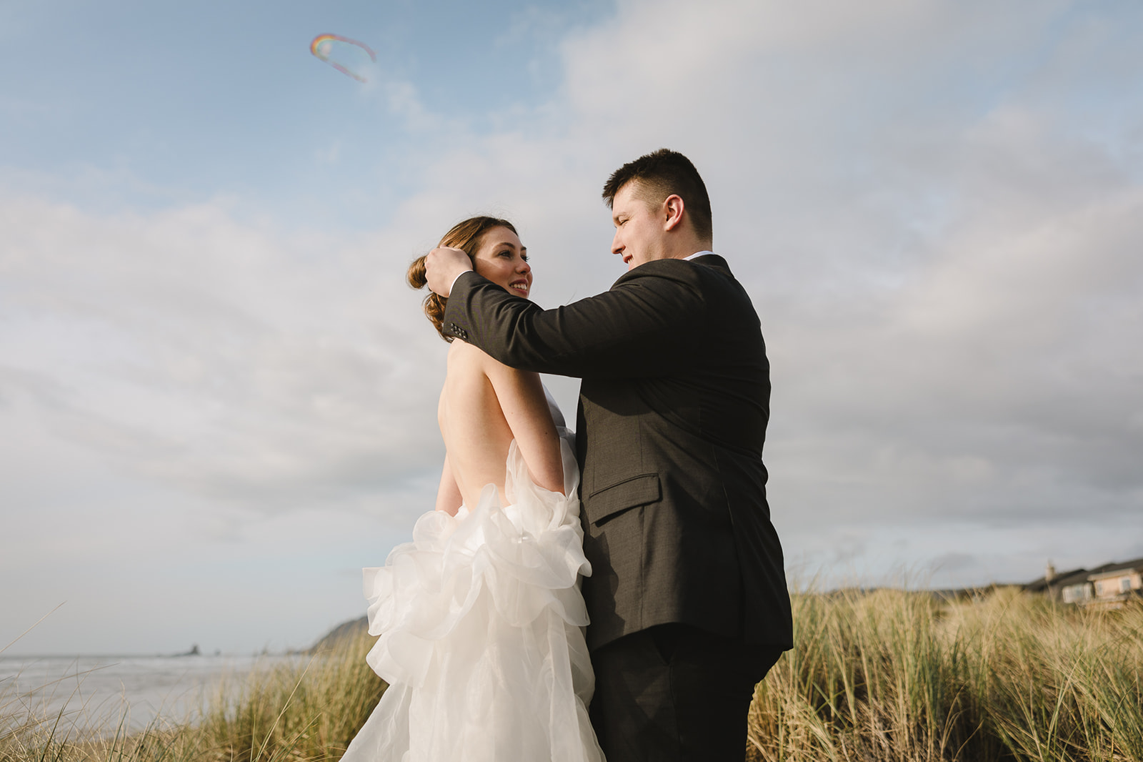 Groom adjusting the brides hair while on the beach.