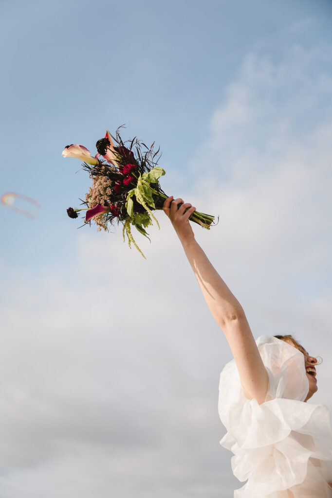 Bride laughing while holding her bouquet by Summit Blooms NW in the air.