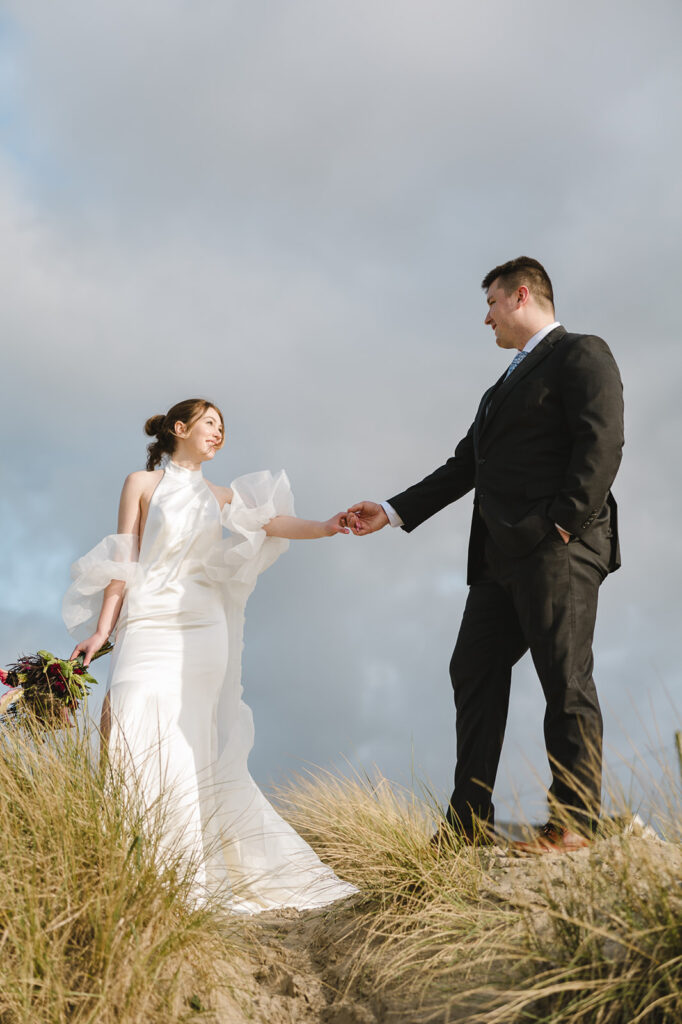 Bride and groom holding hands on a sand dune.