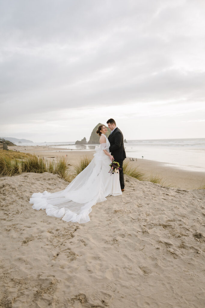 Bride and groom posing on the beach during their Cannon Beach elopement phots with Haystack Rock behind them.