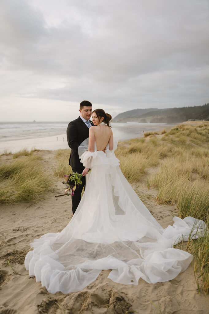 Groom looking at the bride as they pose on Cannon Beach for their elopement photos.