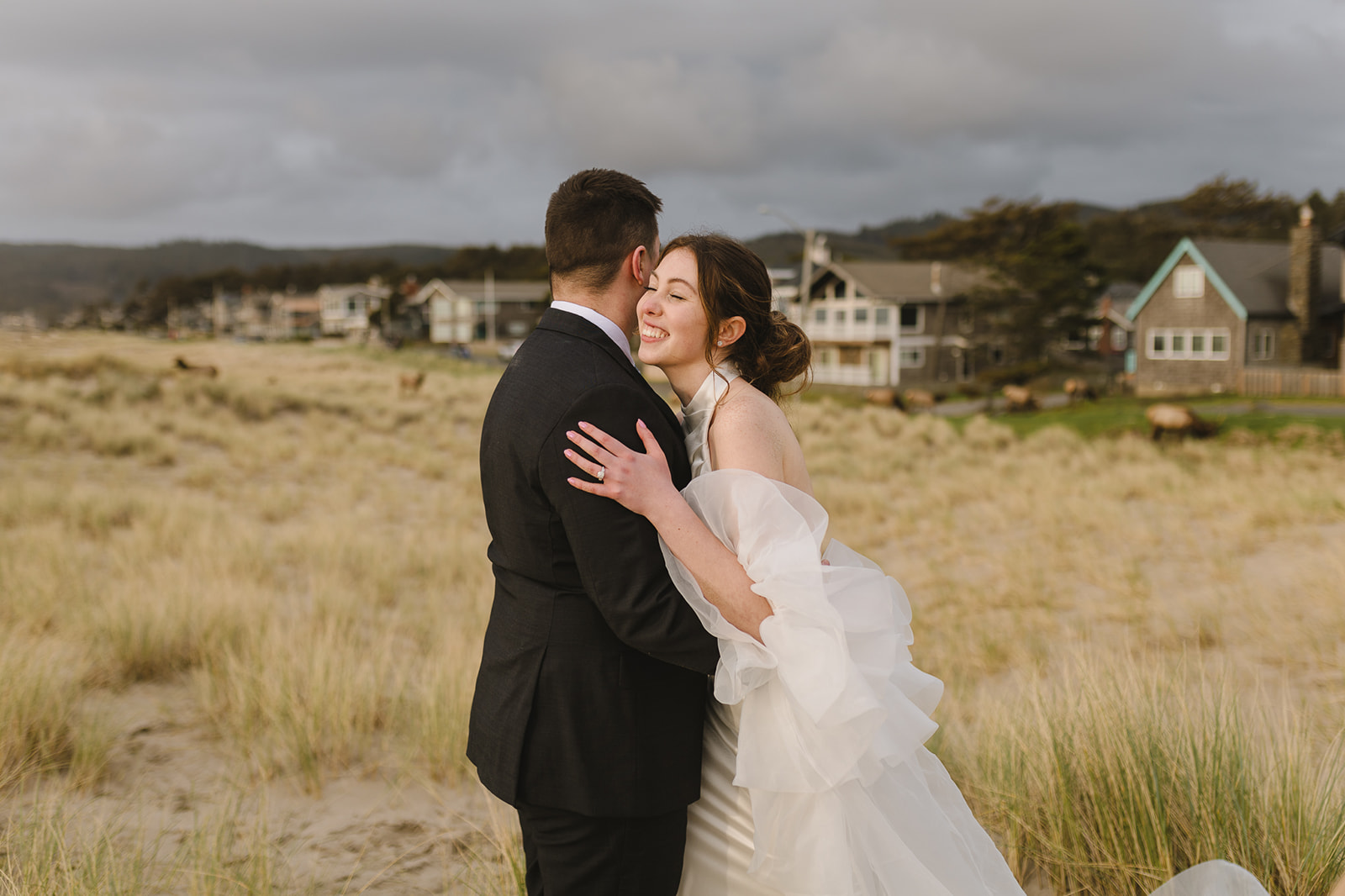 Wide shot of a couple laughing on Cannon Beach with houses in the background.