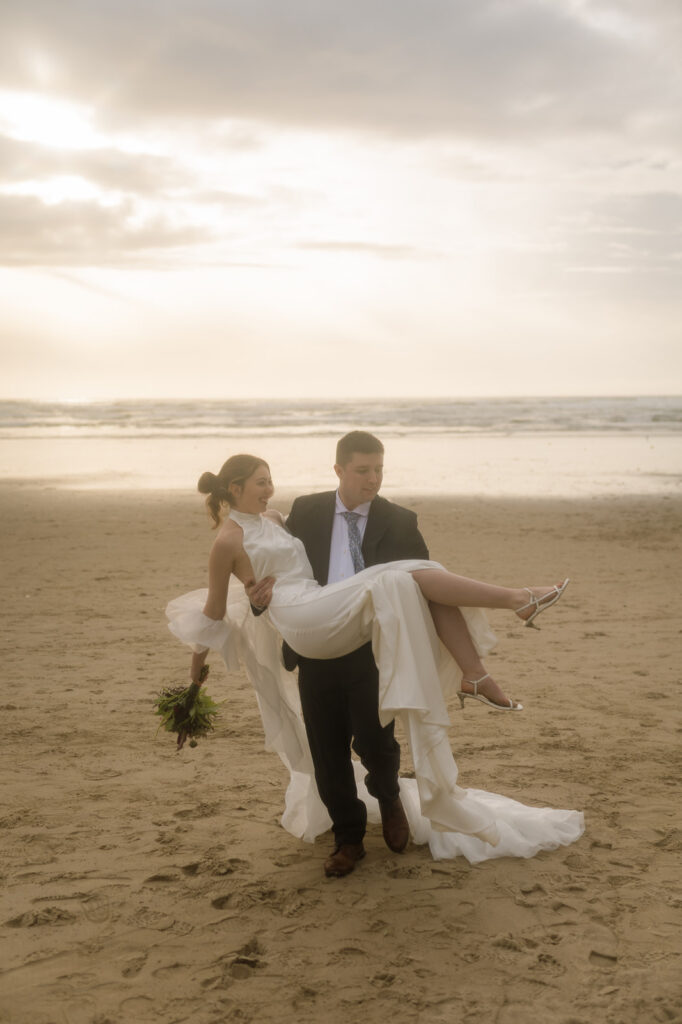 Groom carrying the bride in his arms during their Cannon Beach elopement during golden hour.