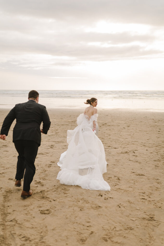 Bride and groom running along Cannon Beach during golden hour.