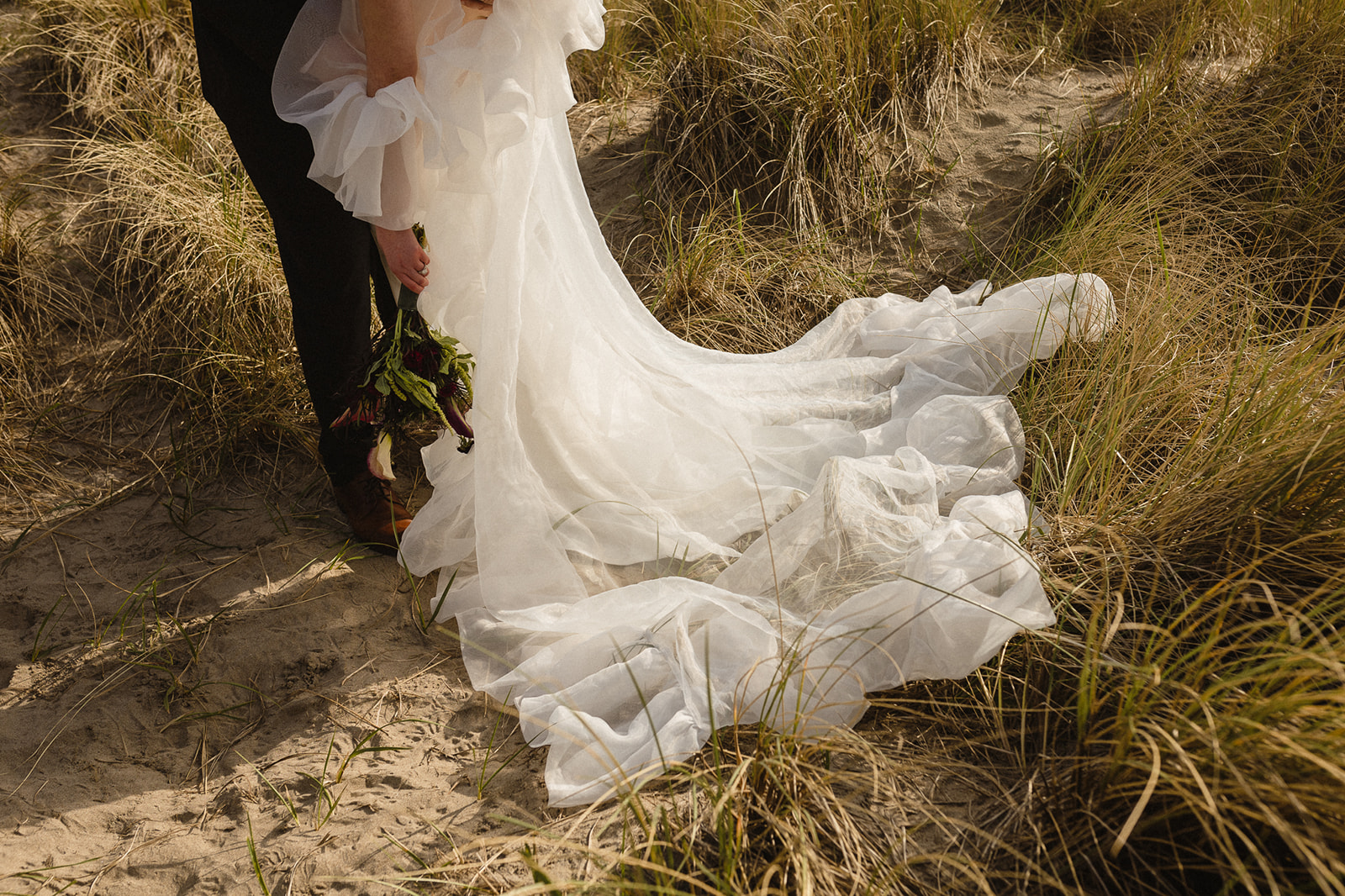 Close up wide shot of a bride and groom standing in beach grass.