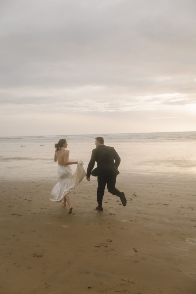 Filmy inspired photo of a bride and groom running along Cannon Beach. 