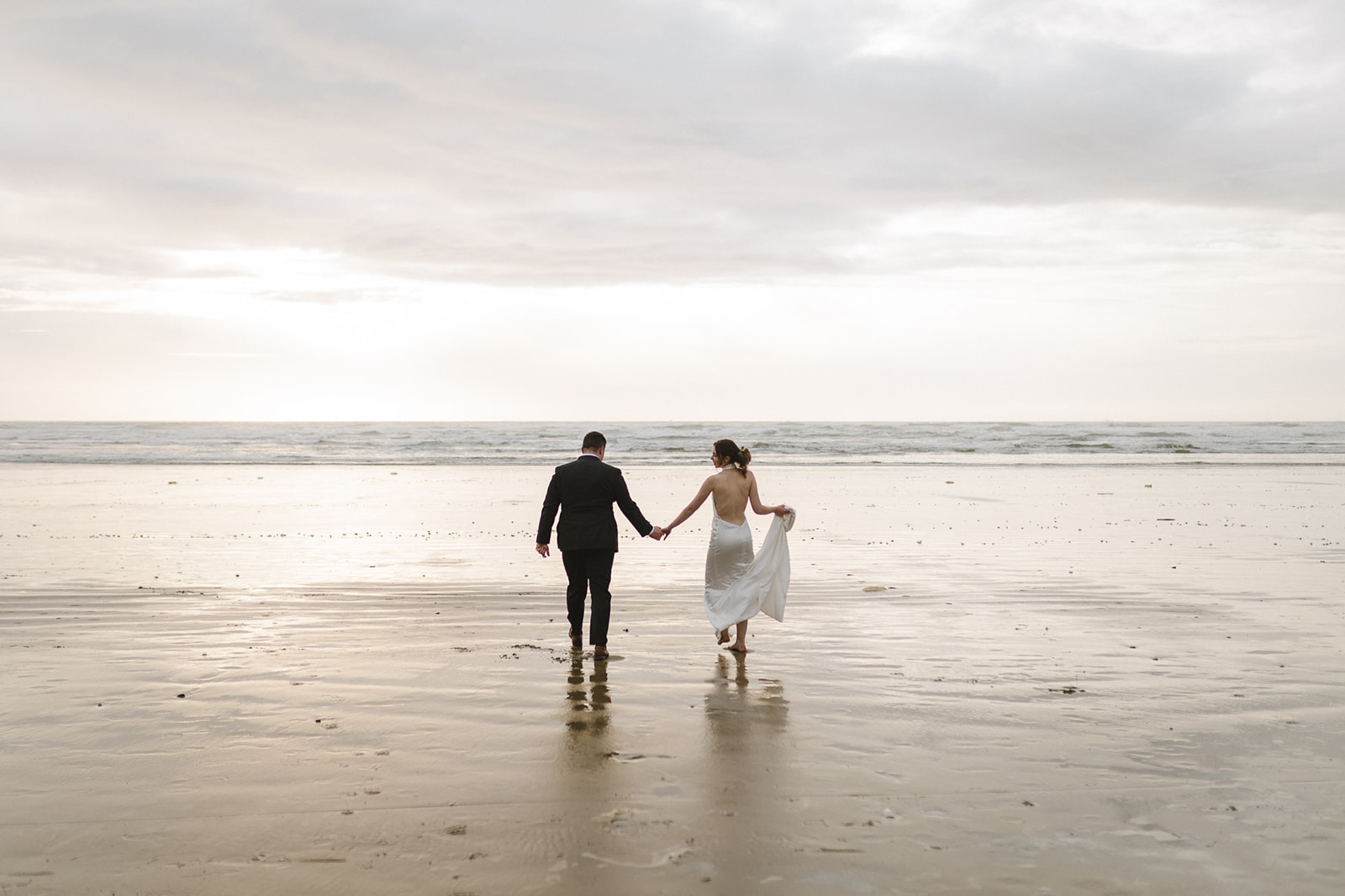 Bride and groom holding hands and walking out to the water for their golden hour elopement photos on the beach.