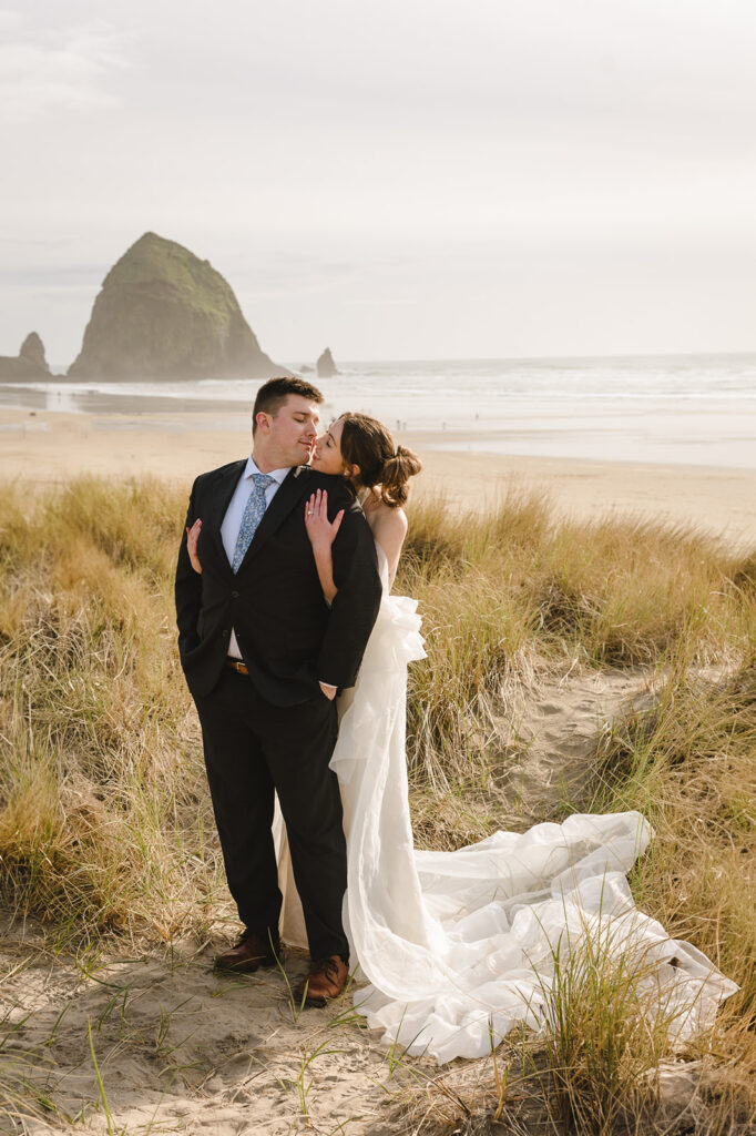 Bride and groom posing on Cannon Beach with Haystack Rock in the distance during golden hour.