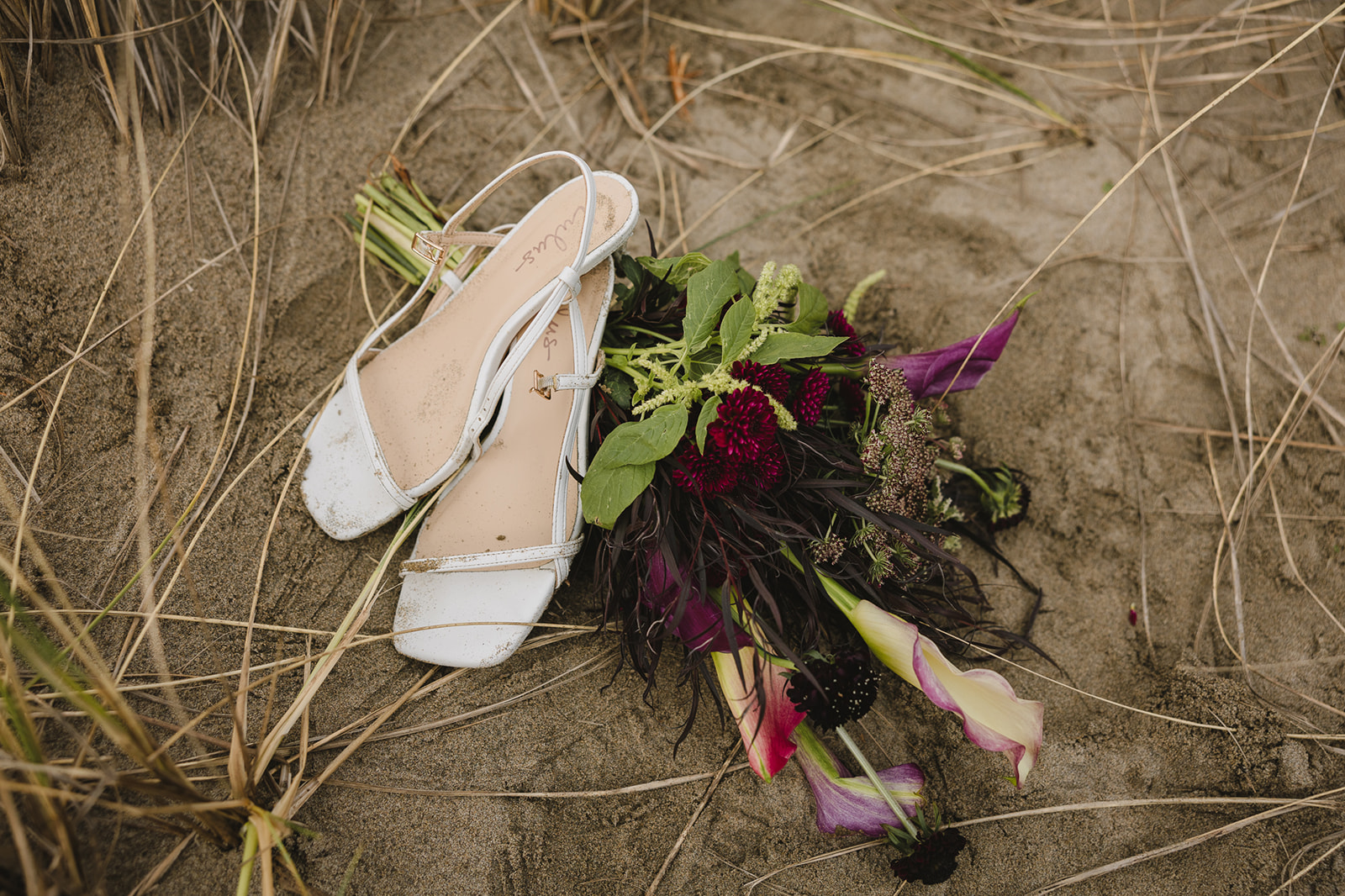 Brides heels and bouquet in the sand for Cannon Bach elopement detail photos.