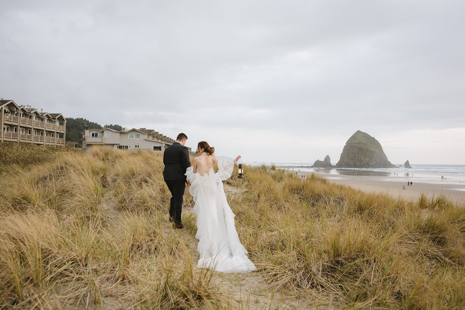 Couple walking along the dunes on Cannon Beach with Haystack Rock in the distance. 