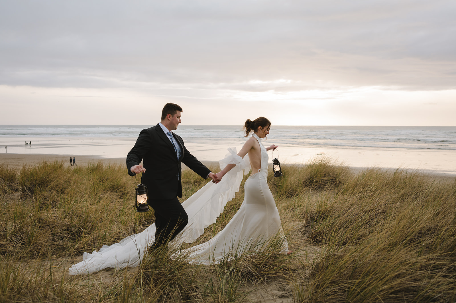Bride and groom walking along the beach grass on Cannon Beach with lanterns.