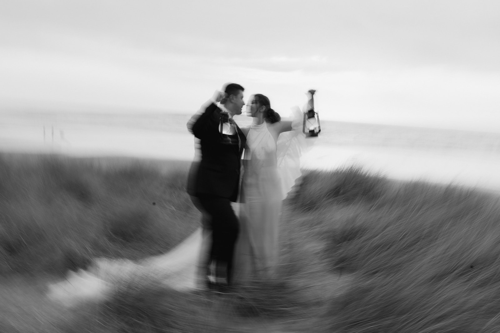 Black and white motion blur photo of a couple holding up lanterns during their Cannon Beach elopement.