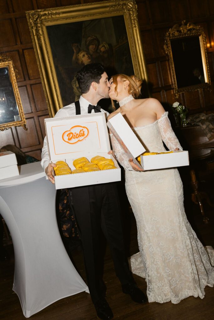 Late night flash wedding reception photography of the bride and groom kissing while holding boxes of Dicks burgers.
