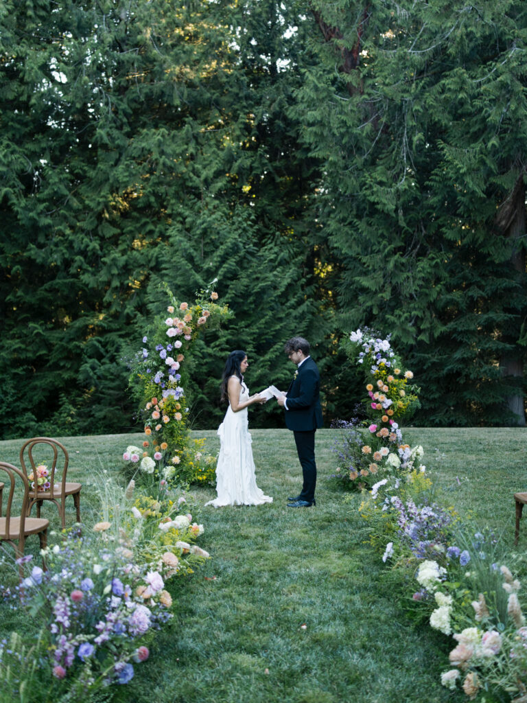 Couple exchanges vows between colorful floral arches on the Amphitheater Lawn at Foxglove Lodge Vashon Island.