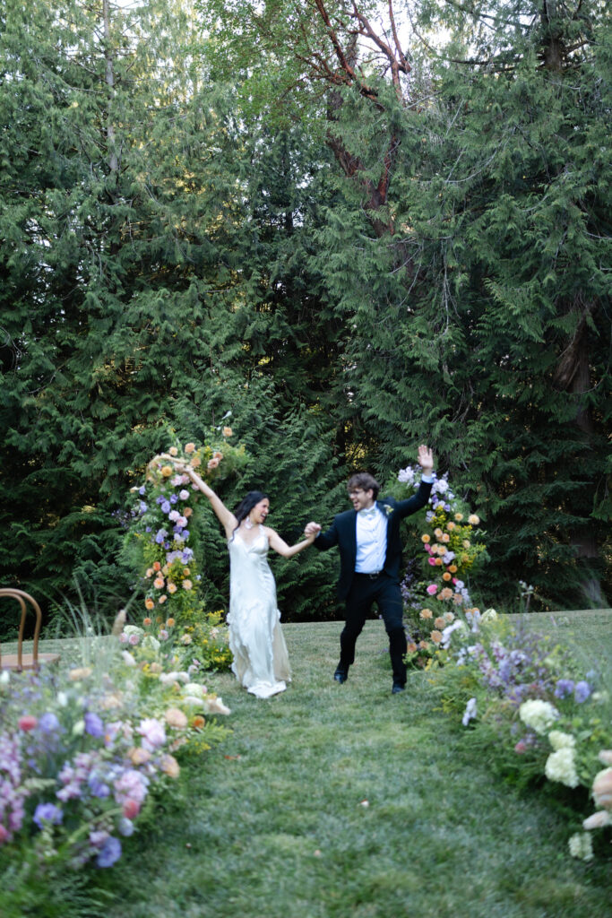 Couple jumping up and celebrating after ceremony on the Amphitheater Lawn at Foxglove Lodge Vashon Island.