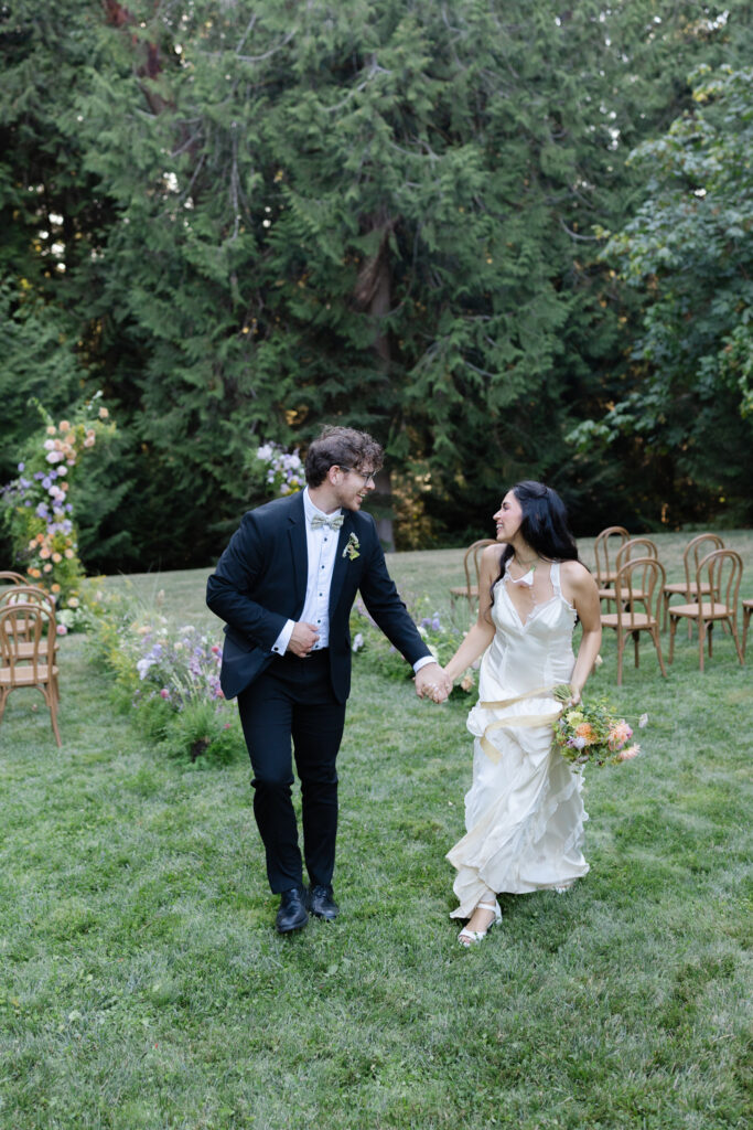 Couple walks hand in hand after ceremony on the Amphitheater Lawn at Foxglove Lodge Vashon Island.