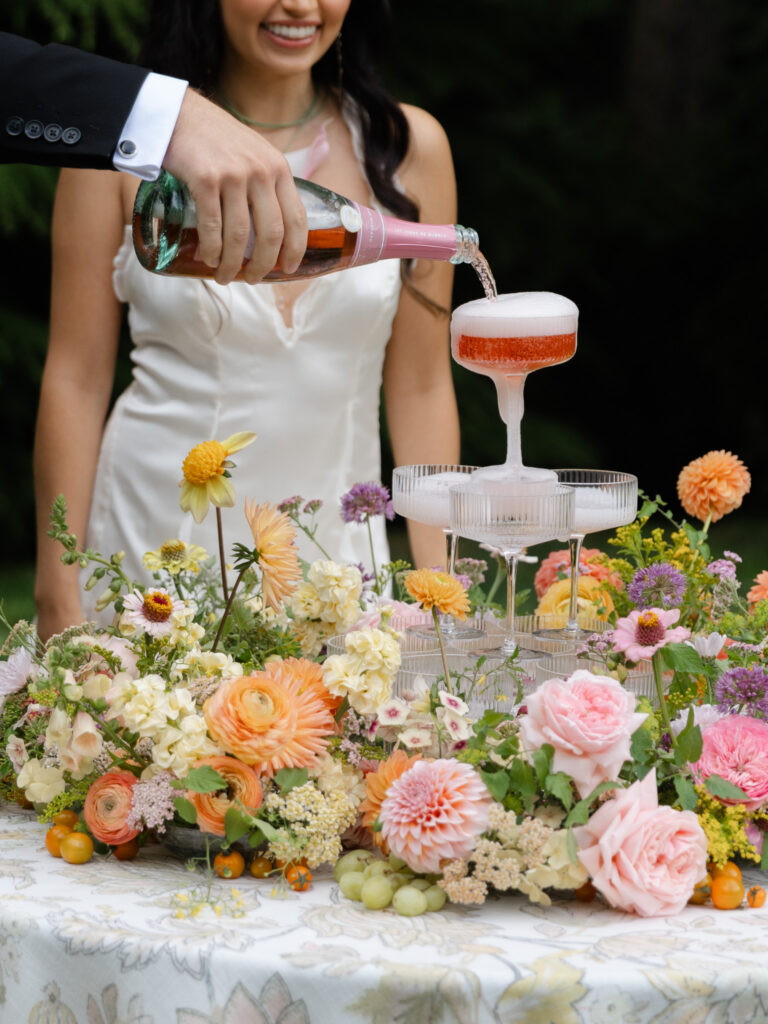 Close up of couple pouring champagne tower with colorful flowers at Foxglove Lodge Vashon Island.