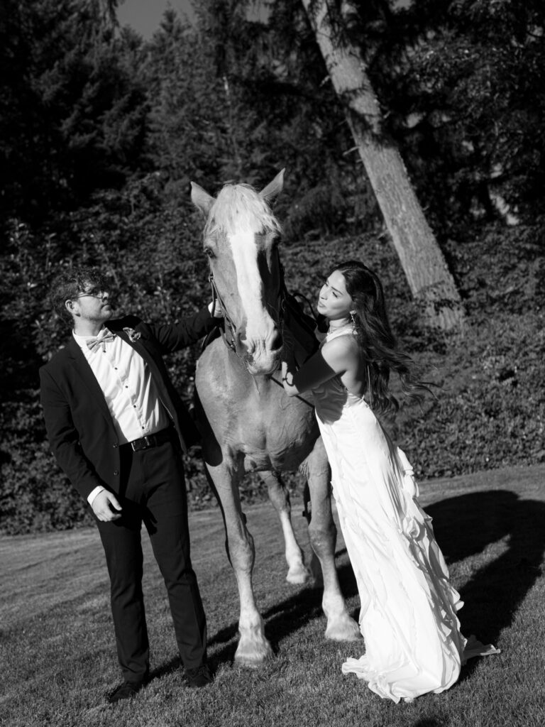 Black and white photo of a couple petting a horse during wedding portraits at Foxglove Lodge Vashon Island.