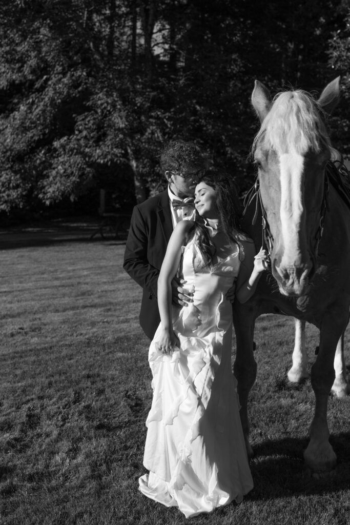 Black and white photo of a couple poses with horse during wedding portraits at Foxglove Lodge Vashon Island.
