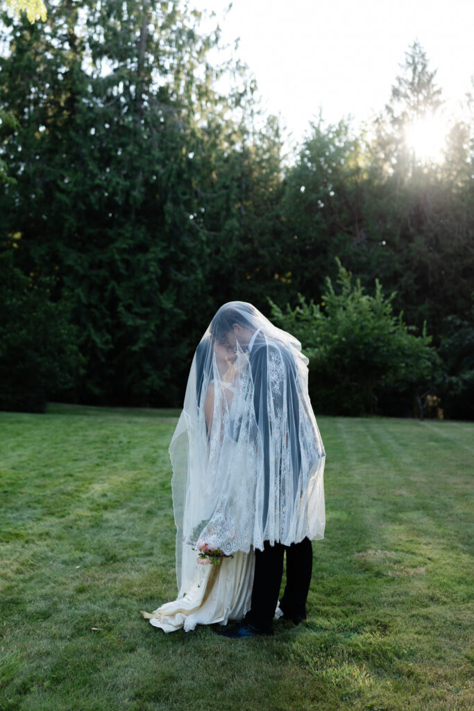 Couple kisses under a veil during golden hour wedding portraits at Foxglove Lodge Vashon Island.