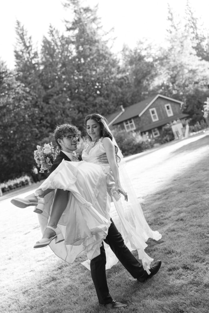Black and white photo of groom carrying bride near Foxglove Lodge Vashon Island.