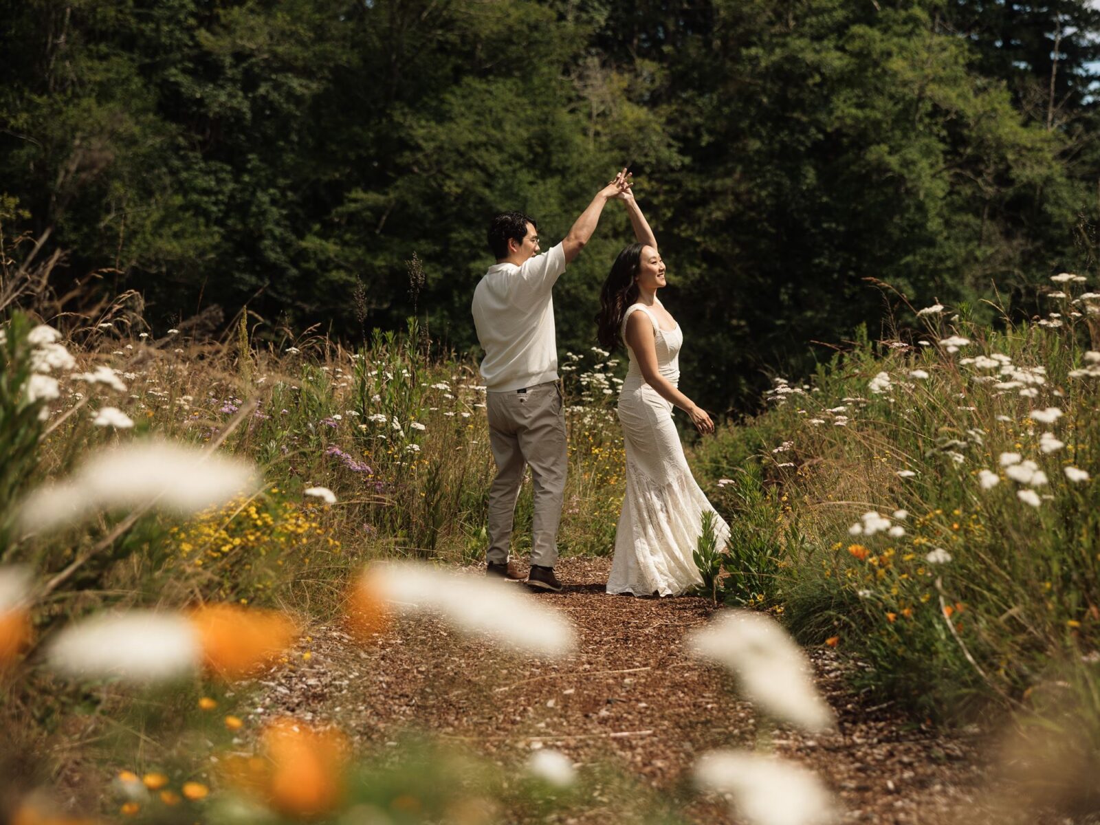 Man twirling his fiancé in a patch of wildflowers.