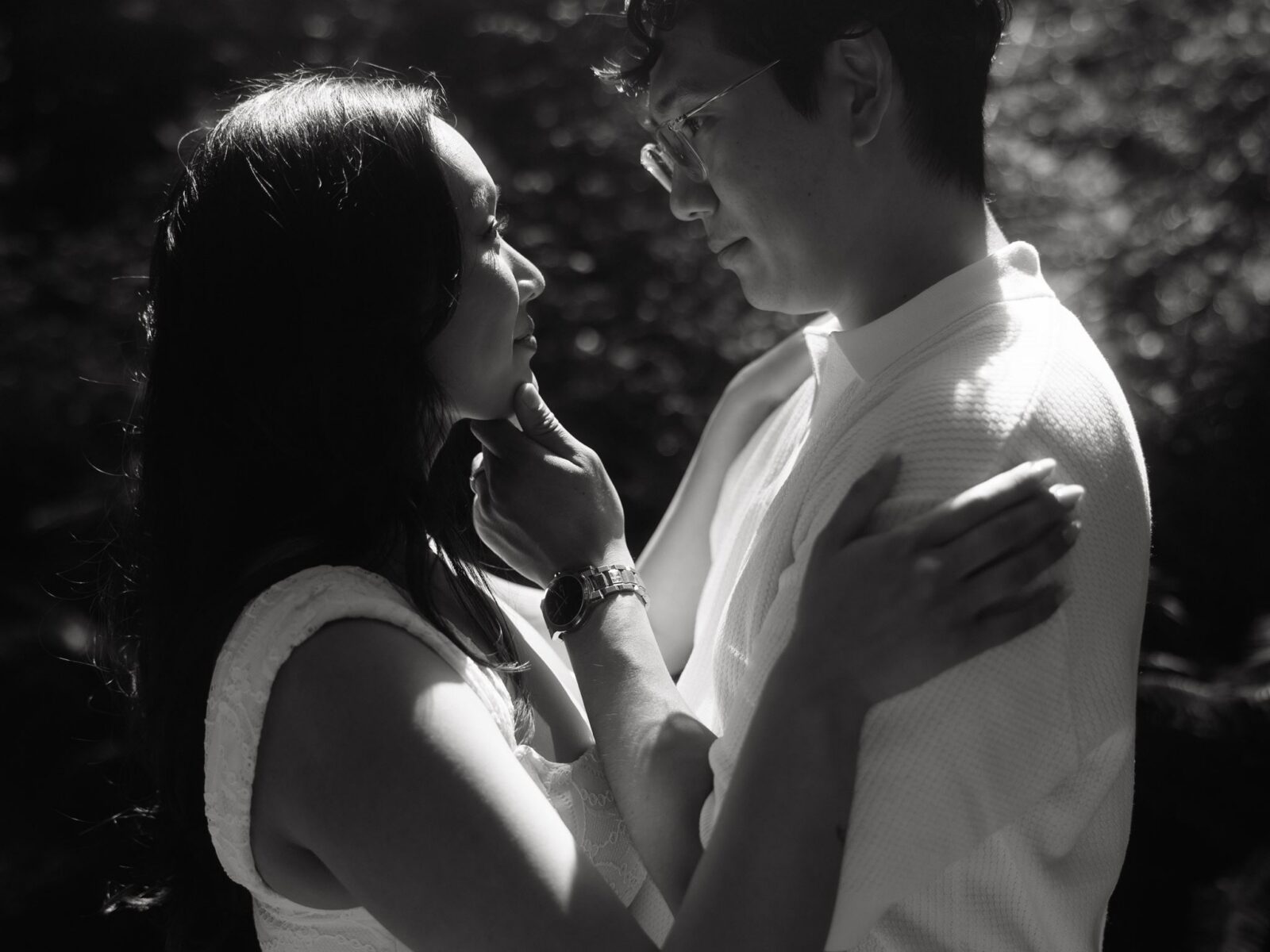 Close up black and white photo of a man caressing his fiancés chin.