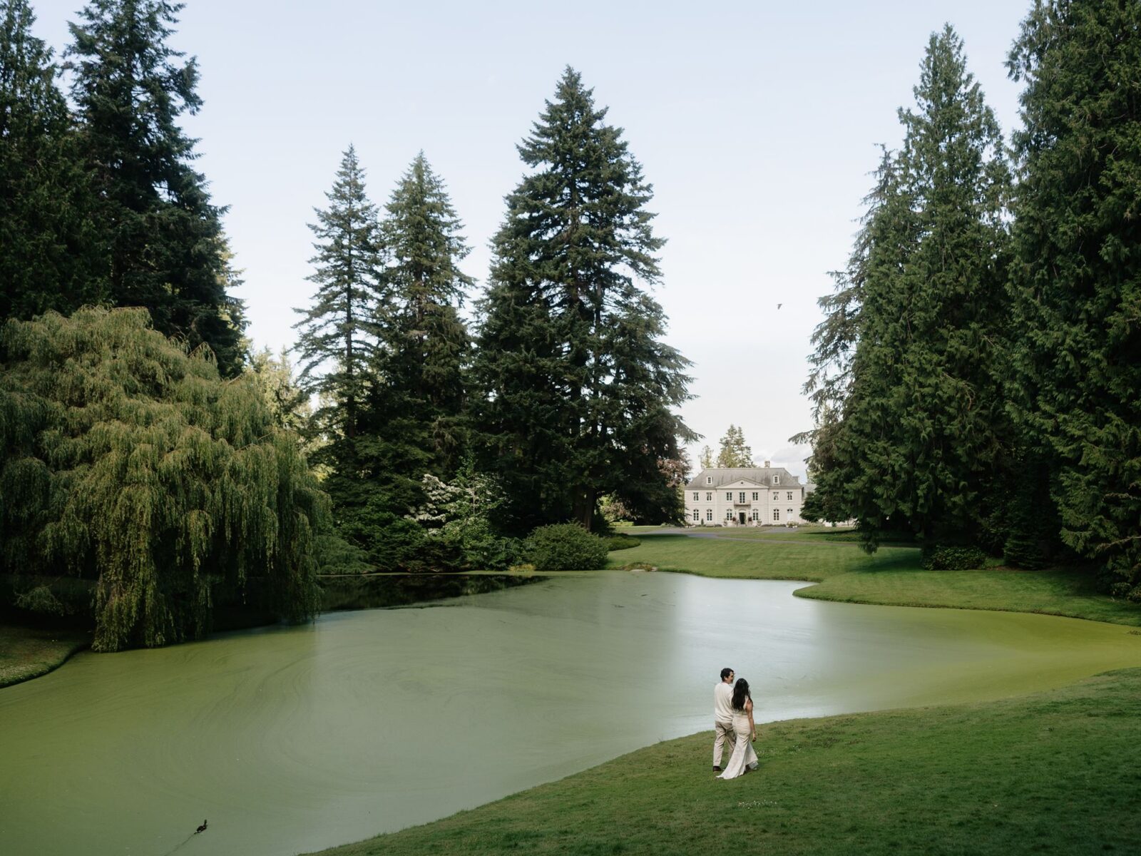 Couple walking near the pond with The Residence in the background.