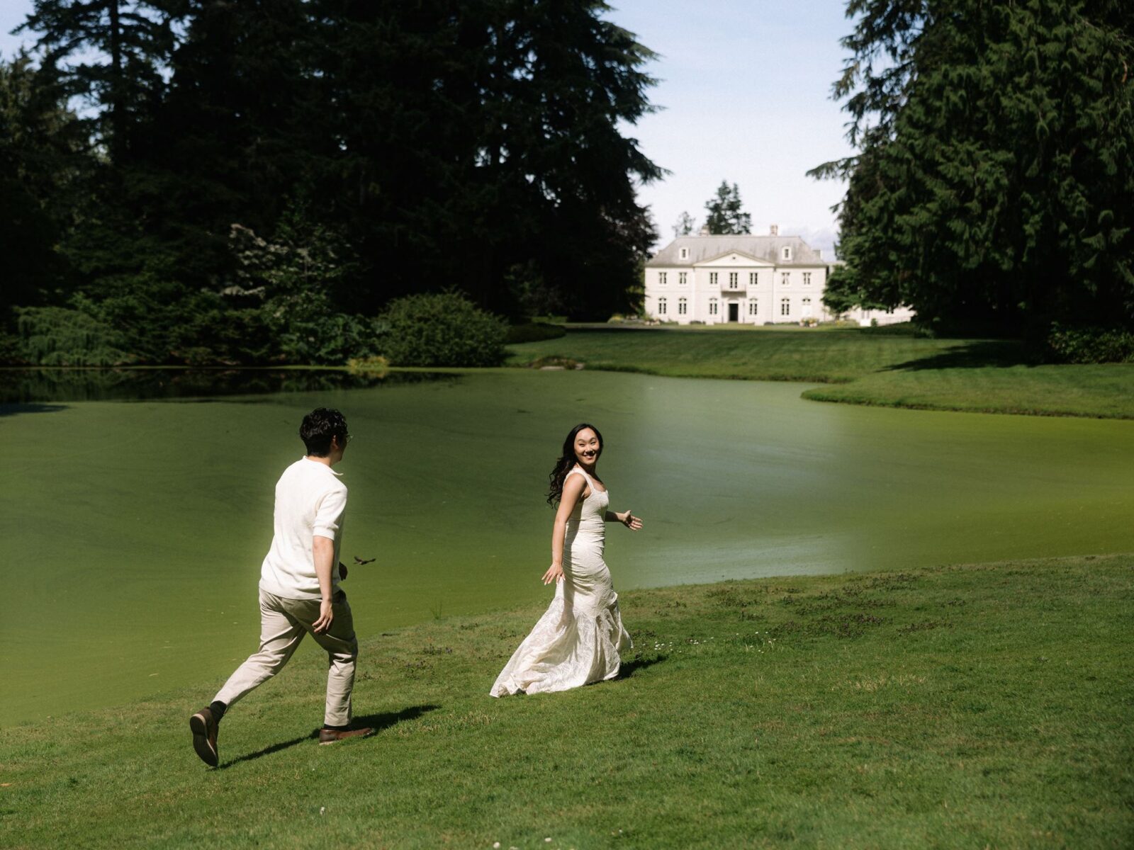 Couple being playful and running along the pond at Bloedel Reserve with The Residence in the background.