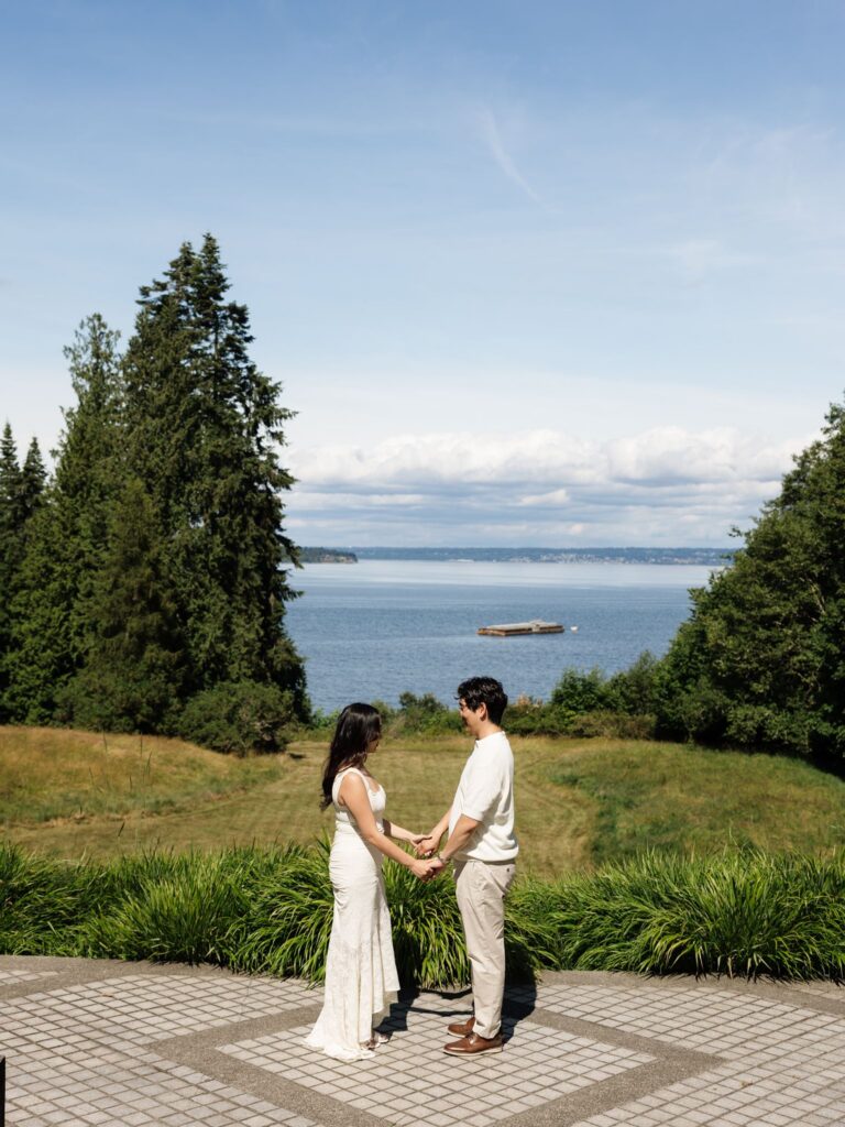 Couple holding hands at Bloedel Reserve with Port Madison in the background.