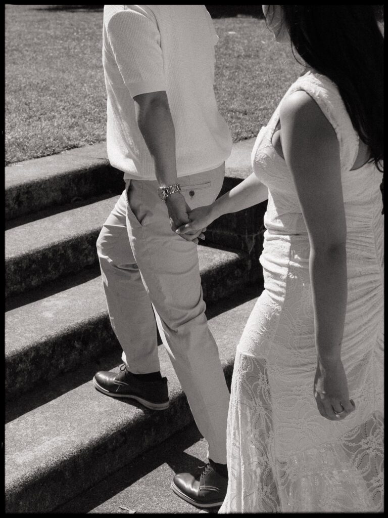 Black and white close up photo of a couple walking hand in hand up a stone staircase.