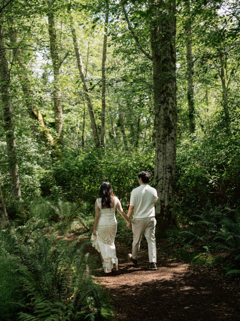 Couple holding hands and walking a wooded path for their Bloedel Reserve engagement photos.