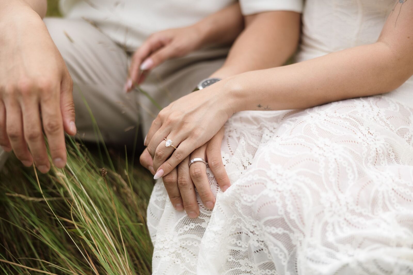 Close up shot of a couple posing in a field while showcasing the woman's engagement ring.