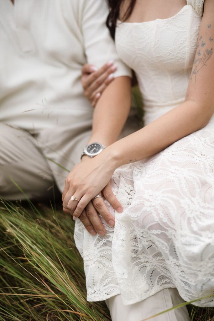 Close up shot of a couple holding hands while showing off an engagement ring.
