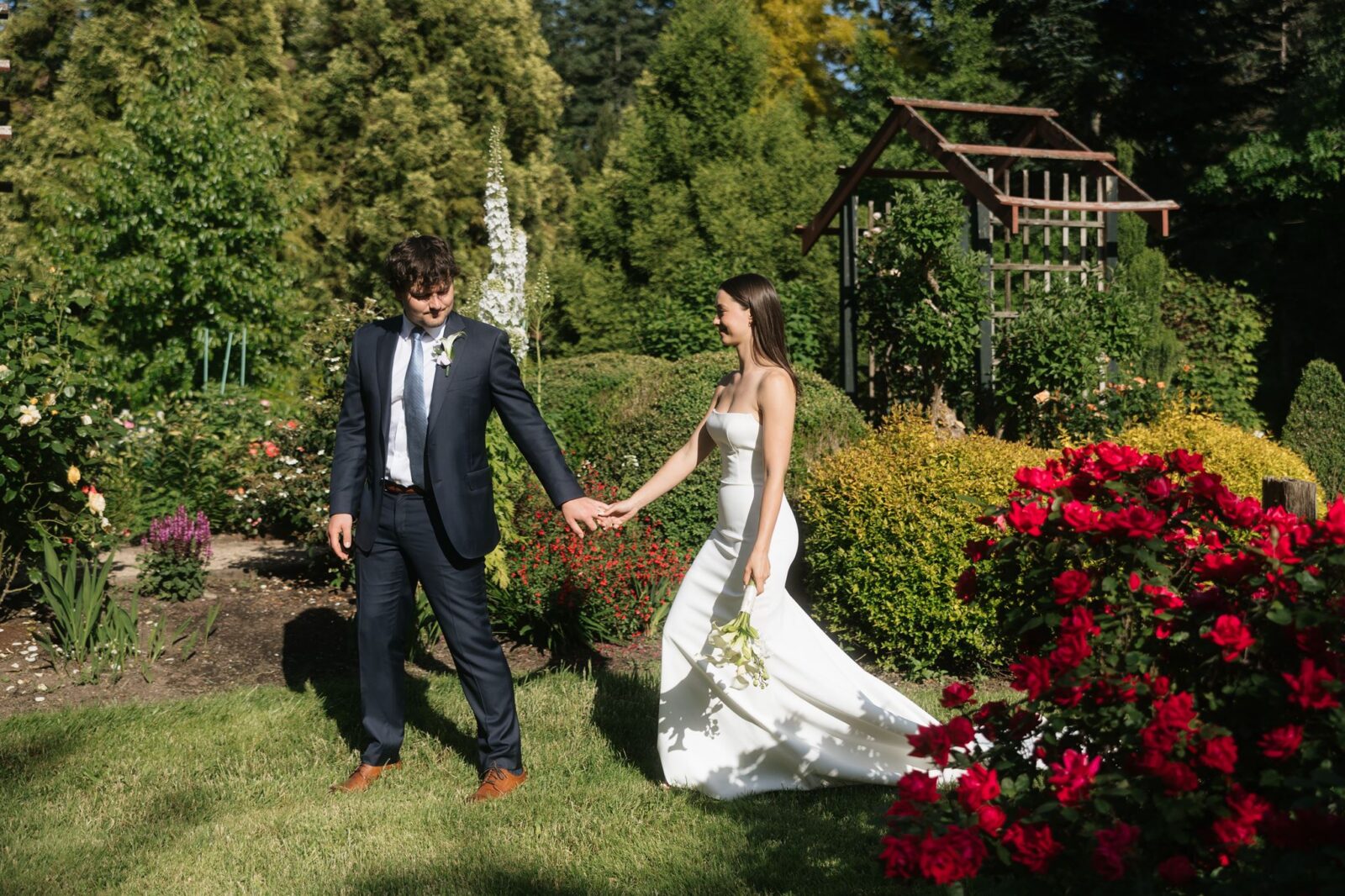 Bride and groom holding hands and walking through Froggsong Gardens in Vashon Island, WA.
