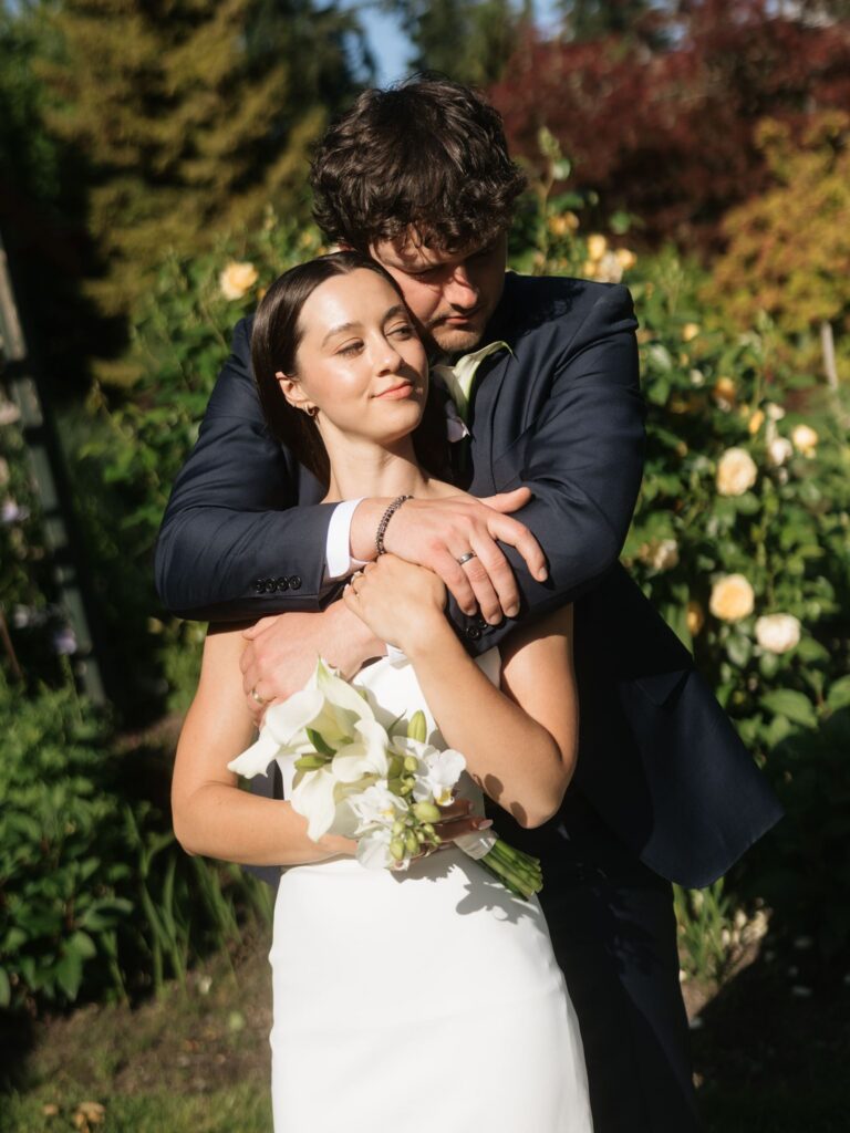 Groom holding the bride from behind during their golden hour portraits at Froggsong Gardens.