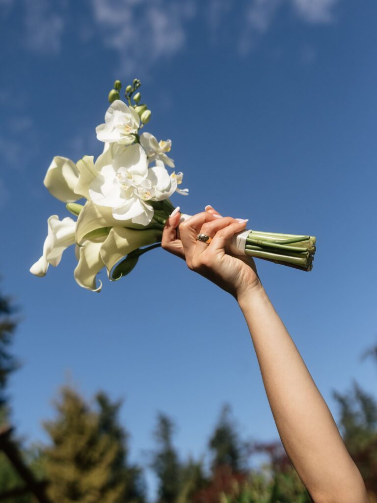 Bride holding a white calla lily and orchid bouquet against a blue sky.